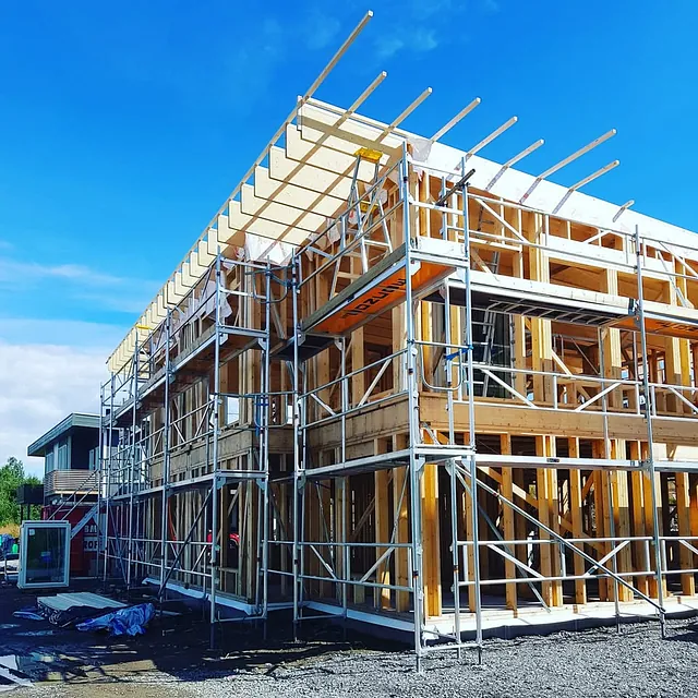 Stillas står rundt et hus under bygging under blå himmel